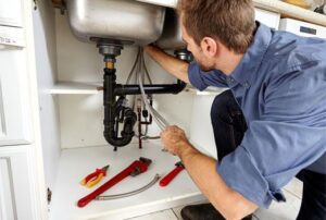 Plumber repairing plumbing under a kitchen sink.